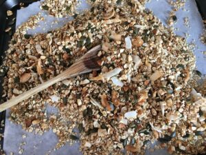 Granola fatta in casa: cucchiaio di legno per mischiare il contenuto a base di fiocchi di avena, cocco, semi misti, mandorle a pezzetti e cosparso di cremina di datteri