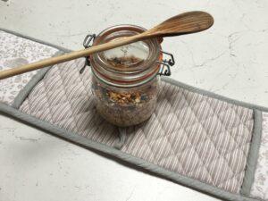 Granola fatta in casa chiusa in contenitore ermetico di vetro con mestolo di legno sopra il barattolo