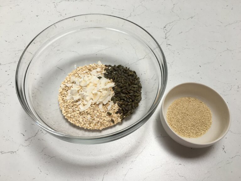 Preparazione granola fatta in casa: ciotola grande di vetro con fiocchi di avena, cocco e semi